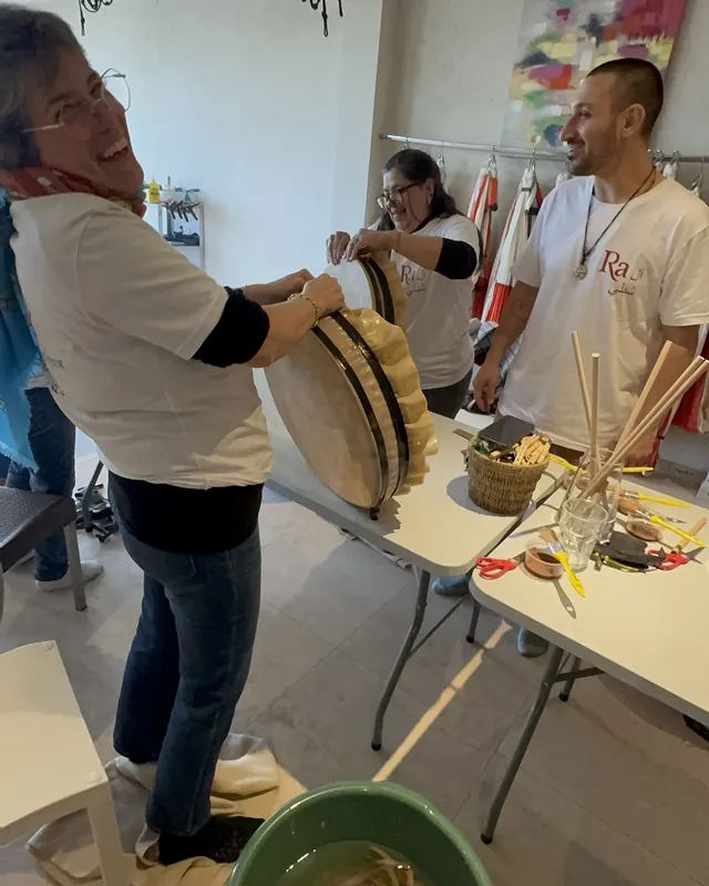 Una alumna riendo mientras sostiene su tambor, con Ra al fondo en el taller de Bernal